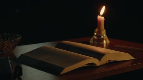 Open Bible Lit by Candle in Dark Room