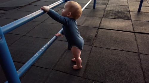 Happy toddler boy stands up on his own using blue jungle gym bars. He stands safely on rubber playgr