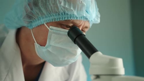 Close Up of Middleaged Doctor in Medical Mask and Hat Looking in Microscope