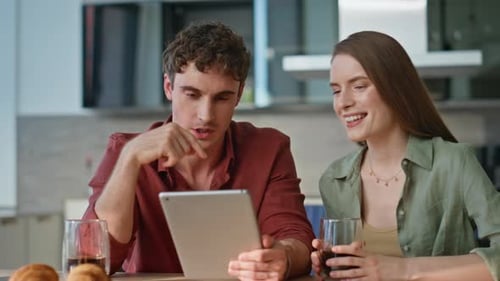 Spouses Discussing Online Purchase at Tablet Sitting Apartment Kitchen Closeup