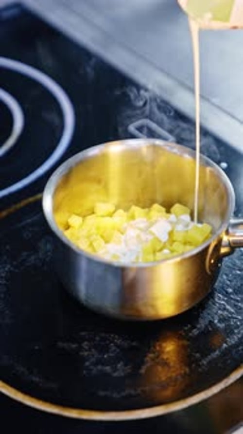 Une poêle avec des pommes de terre coupées en cubes sur le feu. Un cuisinier non reconnu verse la crème dans la casserole
.
