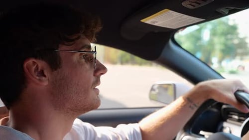 Smiling Young Man Driving His Car Turning the Steering Wheel and Carefully Looking at the Road Side