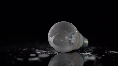 Incandescent tungsten lamp broken on small pieces of glass, isolated on black background