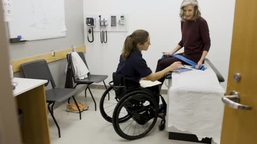 Physical Therapist in Wheelchair Talking with Patient in Clinic Exam Room 3034 Years