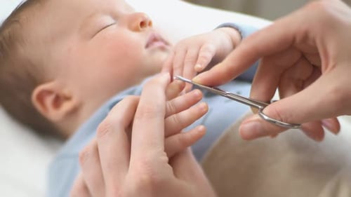Adult Trims Sleeping Infant's Fingernails with Scissors