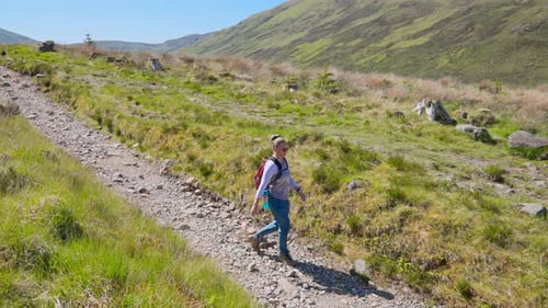 4K Front view of a backpacking hiker walking down a trail through grassy rolling hills on sunny day