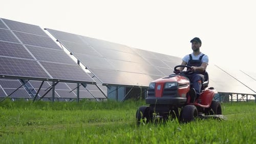 Worker Mows the Grass Near the Solar Panels Green Energy