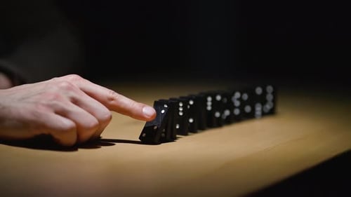 Closeup Pushed Dominoes Falling Down in Line on Wooden Table