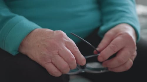 Elderly Woman Adjusting Glasses in Green Teal Sweater Sitting Indoors