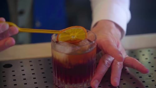 Der Cocktail-Barkeeper bereitet einen Martini mit einer getrockneten Orangenscheibe und Eis zu