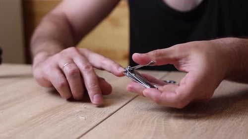Man Clipping Fingernails on Wooden Table Indoors