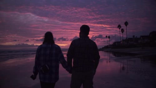Um casal caminha na praia ao pôr do sol