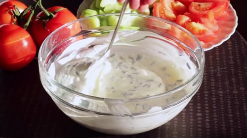 Onion sour cream sauce in glass bowl is mixed with silver spoon, close up