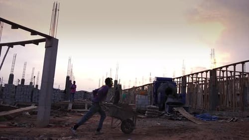 african construction worker pushing sand filled wheelbarrow to concrete mixer at construction site i