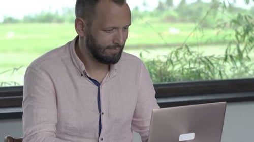 Man Works on Laptop at Table Indoors