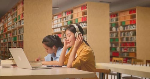 Asiatische Studentin und benutzt Smartphone, während sie mit ihrer Klassenkameradin in der Bibliothek studiert
