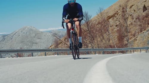 Cyclist from the last effort climbs uphill on a mountain road among high mountains