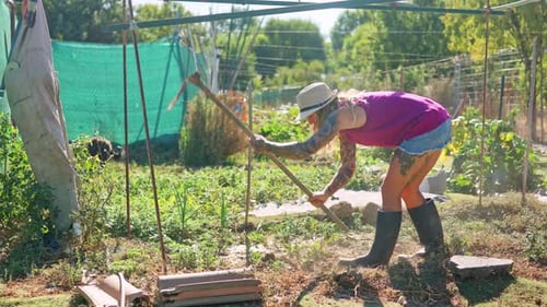 Jardinière tatouée cultivant la terre avec une houe par une journée ensoleillée