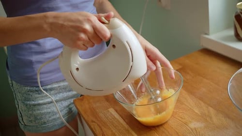 Woman Mixing Egg Yolks in Glass Bowl Using Electric Hand Mixer Preparing Baking Batter Female