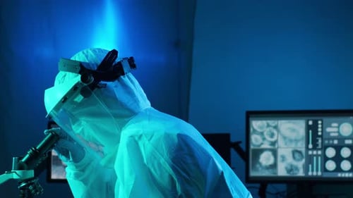 Scientist in Full Body Suit Examining Microscope in Lab
