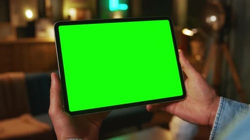 Close Up Hands Holding on Tablet Computer with Horizontal Green Screen Mock Up In the Evening Work