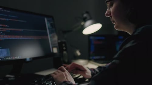À domicile, un programmeur est assis à un bureau encombré de matériel informatique. Concentré sur l'écran