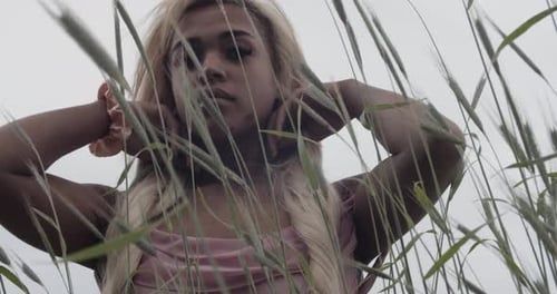 Black Girl With Long Blonde Hair In Pink Gown Standing In Field of Swaying Tall Grass. Close Up.