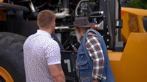 Back View Young and Senior Caucasian Men Talking Examining New Tractor Outdoors Confident