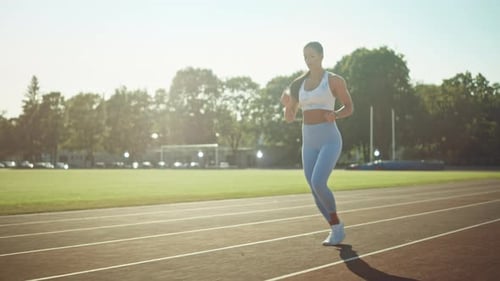 Beautiful Fitness Girl in Light Blue Athletic Top and Leggings Jogging in the Stadium. She is Runni