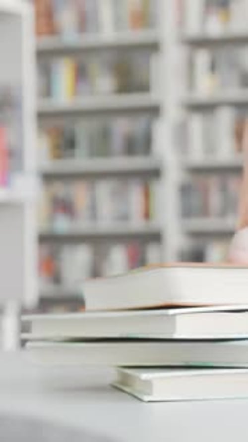 Female Student Reaching for a Book to Join Her Friend for a Study Session in the Library