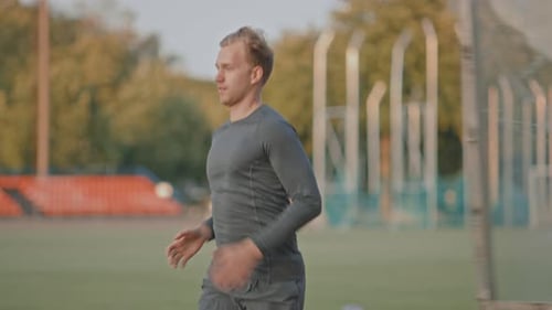 Athletic Fit Man in Grey Shirt and Shorts Jogging in the Stadium. He is Running Fast on a Warm Summ