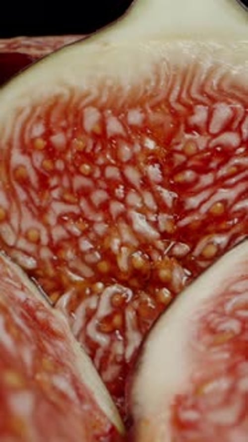 Vertical video. The Camera Moves Across Sliced Halves of Red Figs on a Black Background. Dolly slide