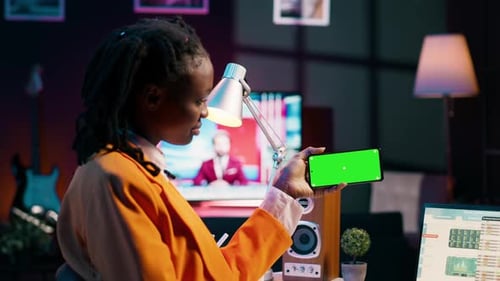 Niña afroamericana sostiene un teléfono con pantalla verde aislada en su casa