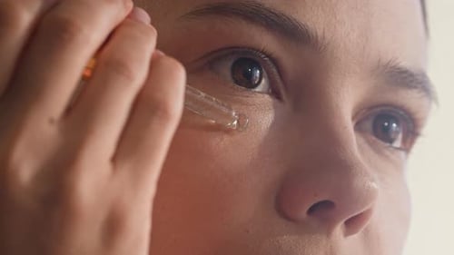 Young Woman Dropping Rejuvenating Serum on Under Eye Zone with Pipette