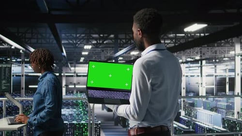 Technicians in Data Center Analyzing Performance Outputs on Green Screen Laptop