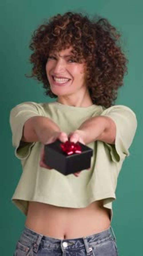 Surprised Woman Opening Gift Box in Green Colored Studio Vertical Orientation