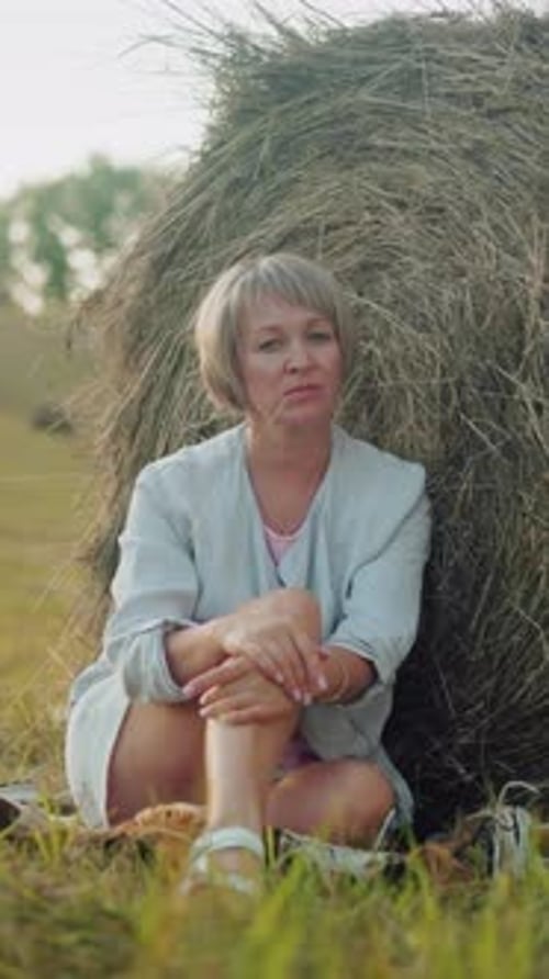 Woman Seated Resting on Hay Bale in Vast Grass Field