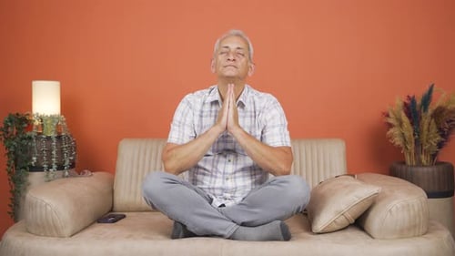 Mature Man Meditating on Sofa in Living Room