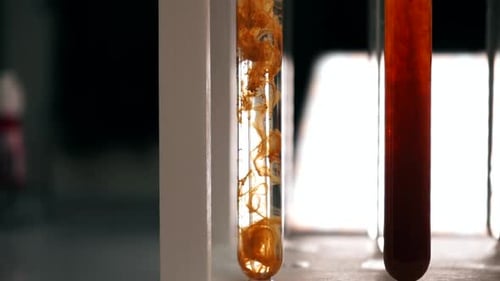 El reactivo químico naranja se disuelve lentamente en un tubo de ensayo con un líquido transparente
