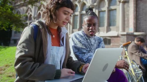Two College Girls Using Laptop and Discussing Project Outdoors on Campus