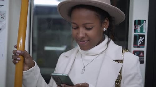 Joven afroamericana feliz de pie usando el teléfono celular en el transporte de pasajeros del metro