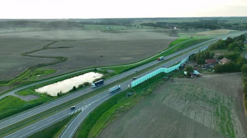 Aerial view of a winding highway passing through green fields and farmlands, with a small pond and s