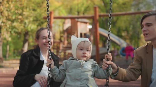Loving Couple Assists Young Child on Winter Playground Equipment Affectionate Parents Guide Their