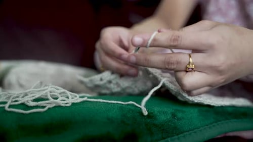 Woman crocheting with white wool sitting on green sofa