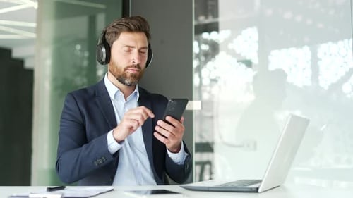Handsome businessman with headphones listening to relaxing music sitting in business office. Happy