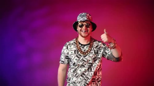 Joyful Eccentric Rich Man in Clothes with Dollars Image with Gold Teeth Showing Thumb Up in Studio