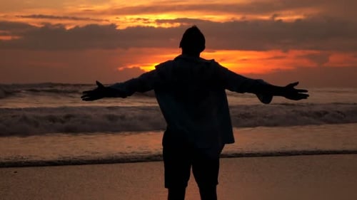 Man Embracing Sunrise on Beach with Arms Outstretched