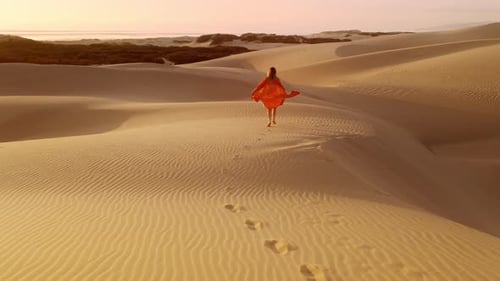 Young Woman in Orange Dress Running Up on Top of Sand Dune at Golden Sunset