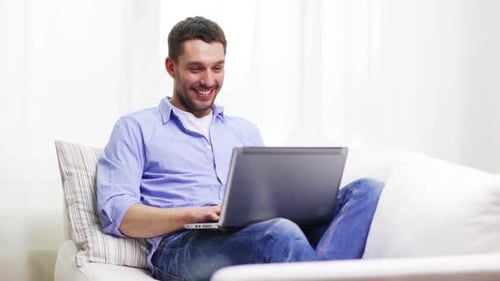 Smiling Man Relaxing on Couch Using Laptop