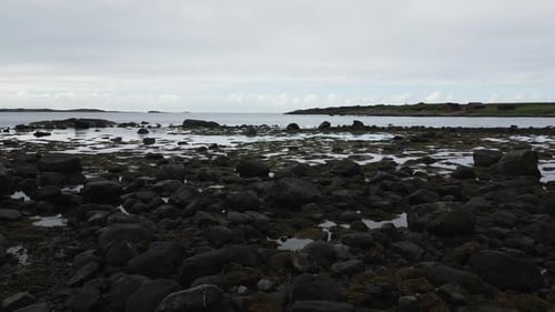 Walking over the stone boulder studded beach in Norway towards the open ocean Fjord at a coastal tra